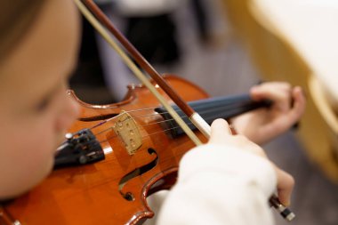 Parlak bir sınıfta, genç bir müzisyen dikkatle keman çalmaya odaklanır. Ahşap aletin sıcaklığı, grup dersinin gevşek atmosferiyle çelişiyor..