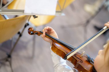 Genç bir sanatçı müzik sınıfında keman çalarken dikkatle konsantre olur. Çevreleyen öğrenciler ve hafif ışıklandırma öğrenmek için sıcak ve odaklanmış bir ortam oluşturur.