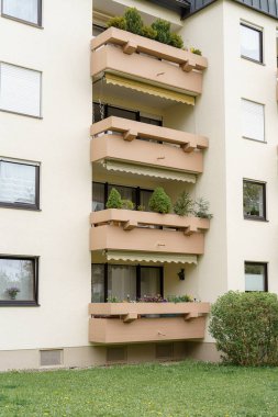 Çağdaş bir apartmanın balkonlarında çeşitli canlı bitkiler sergileniyor. Dış görünüşü temiz bir bahçe düzeni yansıtıyor. Şehir atmosferini güçlendiriyor..