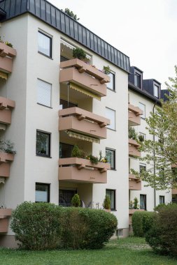 Saksı bitkileri ve çiçeklerle dolu balkonlar modern bir bina üzerinde canlı bir atmosfer yaratıyor. Yapıda temiz hatlar ve kentsel manzarayı geliştiren manzaralı bir alan yer alıyor..