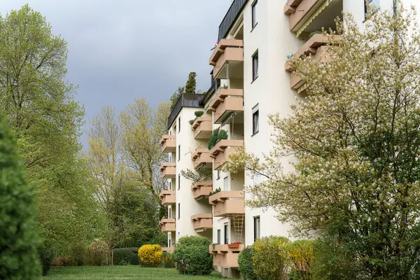 Modern bir apartmanda, zengin bir banliyöde bulunan bitkilerle süslenmiş balkonlar yer alır. Bulutlu gökyüzü huzurlu bahçe alanını kaplıyor, sakin bir atmosferi güçlendiriyor..