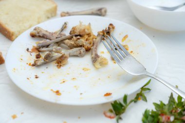 Bir tabak, yanında bir çatal ve etrafında bir parça ekmek ve salata ile tatmin edici bir yemekten sonra kalan tavuk kemiklerini ve yiyecek parçalarını gösterir..