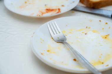 Bir çatal boş bir tabakta duruyor, yiyecek kalıntıları etrafa saçılmış, rahat bir yemek alanında paylaşılan bir yemek deneyiminin altını çiziyor..