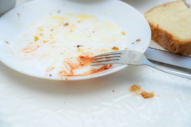 Masada, sos ve kırıntı izleri de dahil olmak üzere kullanılmış bir tabak var. Tabağın yanında bir çatal duruyor ve yakınlarda da bir dilim ekmek var..