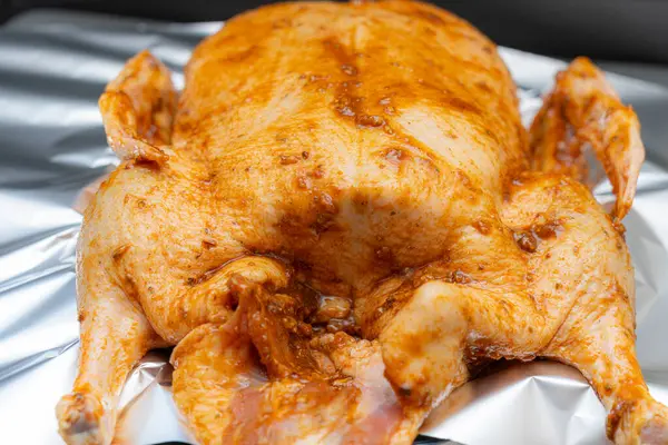 Zengin bir salamura ile kaplanmış bütün bir tavuk mutfaktaki alüminyum folyonun üzerinde oturur. Hazırlık, fırında kızartılmaya hazır baharat ve tatları ön plana çıkarıyor..