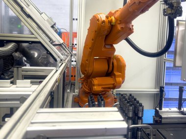 Robot bir kol aktif olarak modern bir üretim ortamında çalışıyor, bileşenleri hassasiyet ve verimlilikle idare ediyor. Ayarlar gelişmiş teknoloji ve otomasyonu yansıtıyor..