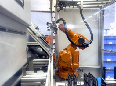 Robot bir kol modern bir üretim tesisinde montaj görevini yerine getirir. Çevre parlak ve gelişmiş otomasyon gösteren ekipmanlarla dolu..
