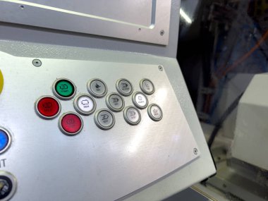 Bir kontrol paneli, atölye ortamında makine yönetiminde tipik olarak başlangıç, stop ve mod anahtarlarını içeren bir dizi düğmeye sahiptir. Parlak ışık, endüstriyel işlevselliği vurguluyor.