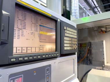 Yoğun bir imalat ortamındaki CNC makine kontrol panelinin detaylı görüntüsü. Ekran, makine süreci sırasında çeşitli ayarları ve etkin programları gösterir.