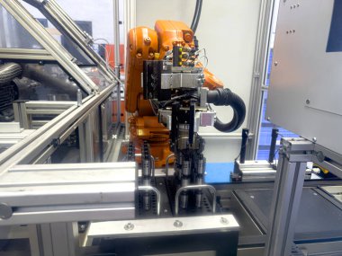 Çeşitli aletlerle donatılmış bir robotik kol, iyi ışıklandırılmış bir imalat tesisi içinde montaj görevleriyle meşgul olur. Kurulumda ileri teknoloji ve hassasiyet çalışmaları sergileniyor.