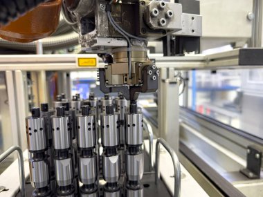 Bir robot kol, benzer elementler arasında yer alırken hassas bileşenleri dikkatlice bir araya getiren bir üretim tesisinde çalışır. Çevre modern ve yüksek teknolojili..