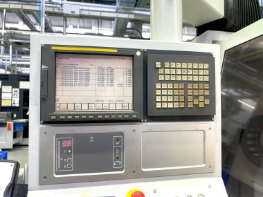 Kontrol paneli modern bir imalat ortamında bir tuş takımı arayüzü ile makine işlemlerinin dijital bir görüntüsünü içerir. Çevre iyi aydınlatılmış, makine detaylarını gösteriyor.