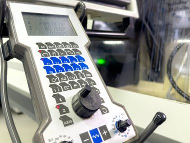 Atölyedeki hassas bir makinenin kontrol panelinin yakın görüntüsü. Panelde çeşitli düğmeler ve üretim süreçlerinin ayrıntılı izlenmesi için dijital ekran yer alıyor..