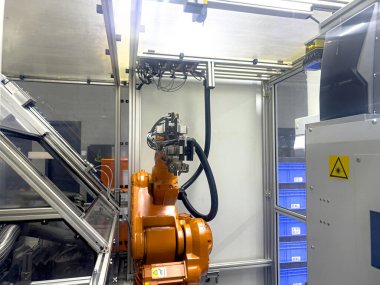 Otomatik üretim tesisinin içine yerleştirilmiş bir robot kol, depolama kutularının arka planına sahip hassas montaj görevleriyle meşgul, yukarıdaki ışıklarla aydınlatılmış..