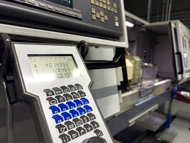Düzenli bir mühendislik atölyesinin içindeki karmaşık bir makine aletinin detaylı kontrol paneline odaklan. Öğleden sonra ışığı özelliklerini ve işlevselliğini vurgular.