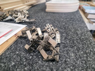 Metal kıskaçlar bir marangozhanenin gri çalışma yüzeyine saçılmış. Bölge, gün boyunca aktif proje çalışmalarını gösteren çeşitli araçlar ve ahşap malzemelerle dolu..