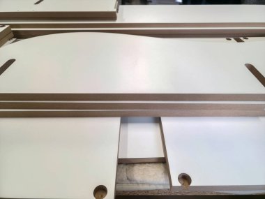 İyi aydınlatılmış bir atölyede, hassas kesilmiş kontrplak çarşaflar bir çalışma tezgahına yerleştirilir. Bu kurulum, devam eden ahşap işçiliğinin, sergilenen zanaatkarlığın karmaşık detaylarını vurgular.