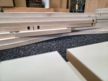 Bir atölyede çeşitli ahşap yapraklar dikkatle istiflenir. Araçlar ve bitmemiş projeler, verimli bir çalışma alanı sergileyerek etrafa saçıldı. Bölgeyi doğal ışık basıyor, detayları arttırıyor..