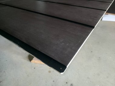 Karanlık paneller, bir iş yüzeyi üzerinde yatay olarak yenilikçi inşaat malzemeleri sergiliyor. Ayarlar, proje inşa etmeye odaklanmış aktif bir atölye atmosferini yansıtıyor.