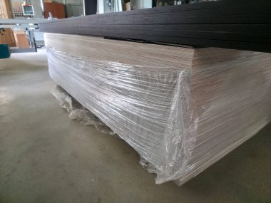 Bir yığın ahşap panel güvenli bir şekilde plastiğe sarılır ve iyi aydınlatılmış bir imalat alanına yerleştirilir. Bölgede son zamanlarda yoğun bir atmosfer olduğunu vurgulayan çalışmalar görülüyor..
