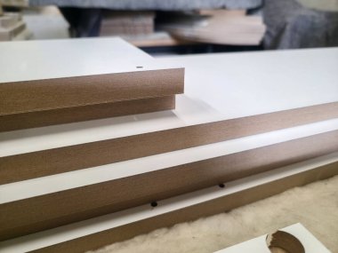 Beyaz yüzeyi ve kahverengi kenarları olan çeşitli lamine çarşaflar marangozluk atölyesine istiflenmiştir. Arka planda araçlar ve malzemeler ile ayar parlak.