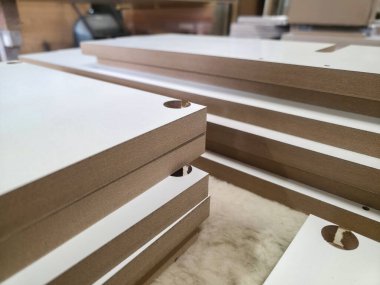 Pürüzsüz, dikdörtgen tahta paneller atölyeye istiflenmiş. Panellerde montaj için kesikler var ve doğal ışık altında zanaatkarlığı sergiliyorlar..