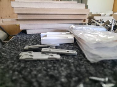 Mobilya parçalarının monte edildiği bir atölye alanı. Tahta ve donanım gibi çeşitli malzemeler görünür olup, aktif işçiliği gösterir.