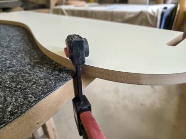 Yetenekli bir marangoz atölyedeki klempi kullanarak hafif bir masa üstünü güvence altına alır. Bu kurulum proje sırasında ayrıntılı ve kaliteli işçiliğe dikkat çekiyor.