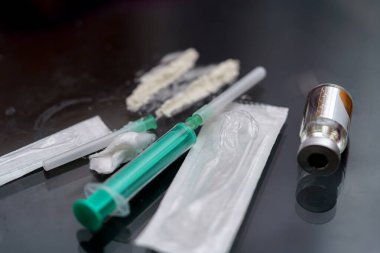 Şırıngalar ve bir şişe de dahil olmak üzere çeşitli tıbbi malzemeler, steril ve klinik yapılarını yansıtan karanlık bir yüzeye yerleştirilmiştir..