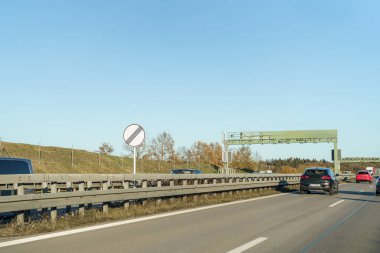 Her iki tarafında bariyerler olan araçlar otoyol boyunca ilerliyor. Yol kenarında giriş yasak tabelası var ve yakında sonbahar renklerinde ağaçlar var..