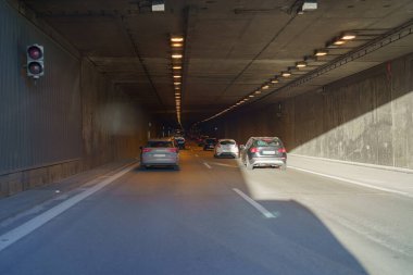 Araçlar gün boyunca iyi aydınlatılmış bir otoyol tünelinde dolaşarak çeşitli trafik lambası sinyallerini gösteren araçlar sergiliyorlar. Atmosfer kentsel ve dinamik..