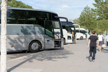 Bir grup gezgin, canlı bir şehir parkında park halindeki otobüslerin yanındaki patikada yürürken, öğleden sonraları sıcak güneşin ve açık gökyüzünün keyfini çıkarıyorlar..