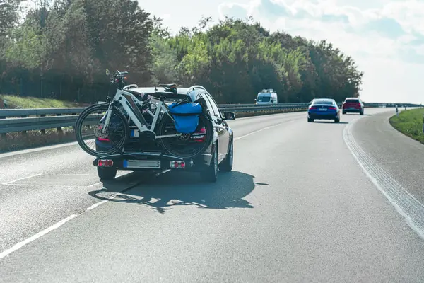 Otoyol boyunca bir araba sürüyor, arka rafa güvenli bir şekilde bağlanmış bisikletleri gösteriyor. Açık gökyüzü ile aydınlık, güneşli bir gün, açık hava maceralarını ima ediyor..