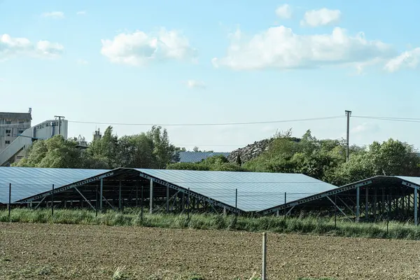Açık bir alandaki bir dizi metal yapıya güneş panelleri monte edilir. Uzakta, depolama tesisleri açık bir gökyüzüne karşı görünür..