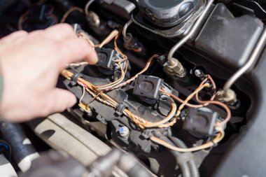 Parmaklar, bir garajdaki karmaşık otomotiv bakımının detaylarını vurgulayarak, bir motorun elektrik bağlantılarını ve kablolarını dikkatle inceliyor..