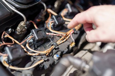 Bir profesyonel arabanın kaputu altındaki elektrik bağlantılarını dikkatlice inceler, atölyenin rutin bakımı sırasında tüm bileşenlerin düzgün çalışmasını sağlar..