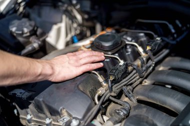 Bir el, garajdaki bir aracın motor bileşenlerine nazikçe dayanır. Bir araba meraklısı gün boyunca her şeyin düzgün çalıştığından emin olmak için motoru kontrol eder..