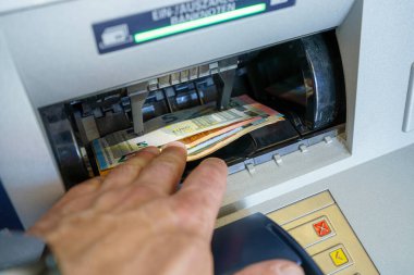 Bir el, hareketli bir şehirde banknotları toplamak için otomatik veznedara uzanıyor. Çevre, gündüz vakti yoğun bir finans bölgesi olduğunu gösteriyor..