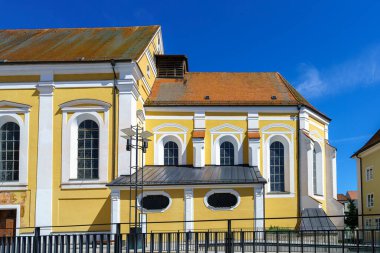 Açık mavi gökyüzüne karşı dik duran tarihi sarı kilise, huzurlu bir kasaba atmosferinde zengin tarihini gözler önüne seren geniş pencereler ve detaylı mimariye sahiptir..
