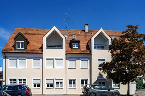 İyi korunmuş bir konut binasında mimari unsurların uyumlu bir karışımı bulunur. Açık mavi gökyüzü, çatıdaki kiremitleri ve düzgünce yerleştirilmiş pencereleri vurguluyor..