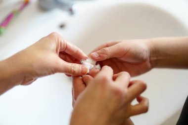 İki el banyodaki küçük, narin bir nesneye odaklanır. Bir kişi diğerine hassas bir görev için yardım eder. Günlük hayatı ve özeni gösterir..