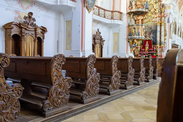 Tarihi bir kilisenin içinde, ahşap sıralar karmaşık oymalar sergiliyor, dönemin işçiliğini yakalıyor. Güneş ışığı kutsal mekanı aydınlatır, ruhsal atmosferini güçlendirir..