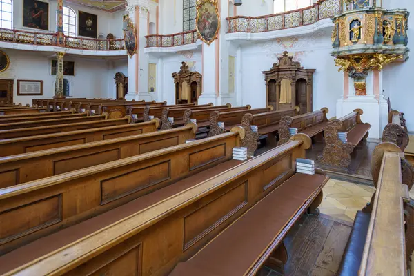 Tarihi bir kilisenin içinde, ahşap sıralar düzgünce dizilmiş duruyor. Güneş ışığı pencerelerden akar, mimarinin süslü detaylarını aydınlatır ve barışçıl bir atmosfer yaratır..