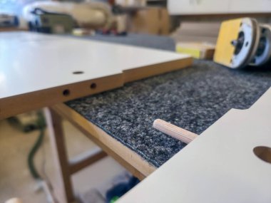 Aletlerle dolu bir atölyede beyaz ahşap paneller toplanıyor, mobilyaların dikkatlice ve titizlikle hazırlandığı yoğun bir ortam sergileniyor..