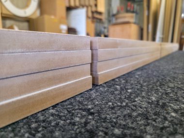 Yoğun bir atölyede, karanlık bir yüzeyde düzgünce istiflenmiş ahşap tahtalar. Tahtanın doğal dokusu görülebilir, bu da çeşitli inşaat projelerine hazırlık olduğunu gösterir..