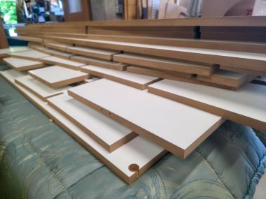 Çoklu ahşap tahtalar bir atölyede yatay olarak istiflenir. Kurulum bir marangozluk projesine hazırlandığını gösteriyor. Doğal ışık boşluğu aydınlatır..