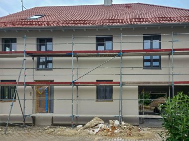 İşçiler, yenilenme sırasında bina güvenlik ve erişim için iskeleyi sararken, yeni kaplamalı bir konut binasının dış yüzeyini yenilemekle meşguller..