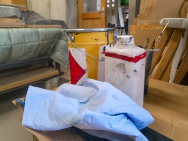 Boya kapları ve eldivenli bir el de dahil olmak üzere çeşitli araç ve gereçler atölye ortamında aktif bir yaratıcı süreci gösteren bir çalışma tezgahına yerleştirilmiştir..