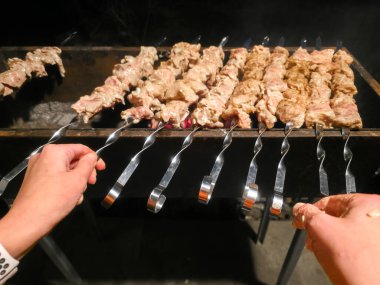Elleri ustalıkla terbiye edilmiş et şişlerini ızgaranın üzerine yerleştiriyor, yazın açık havada yapılan barbeküde havayı dolduran lezzetli bir koku yaratıyor..