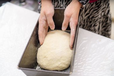Parlak bir mutfakta iki el hamur topunu fırın tepsisinin içine bastırıp şekillendirir. Ellerdeki un, gevşek bir öğleden sonra pişirme sürecine kırsal bir dokunuş ekler..